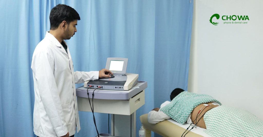 Physiotherapy for back pain with therapist setting electrotherapy machine for patient at Chowa